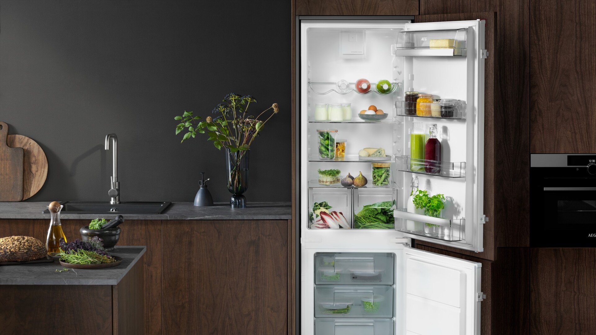 Een donkere keuken met een ingebouwde koelvries-combinatie van AEG die open staat en gevuld is met eten.