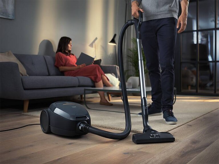 Een vrouw leest terwijl een man stofzuigt.