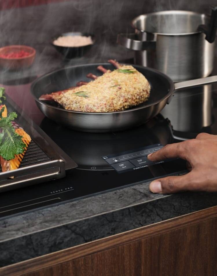 Een vinger raakt het bedieningspaneel van een inductiekookplaat aan terwijl het eten wordt bereid.