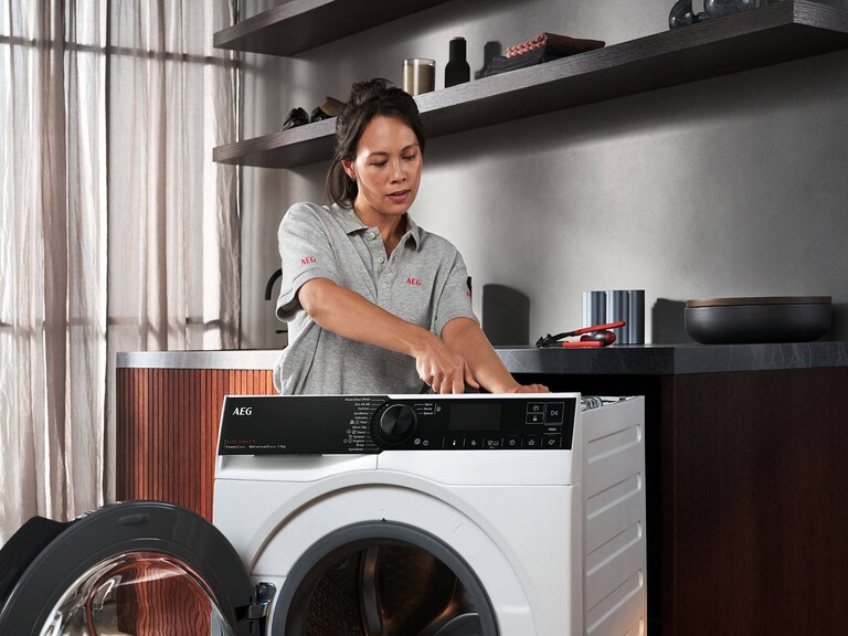 Monteur die een wasmachine herstelt met donkergrijze planken op de achtergrond