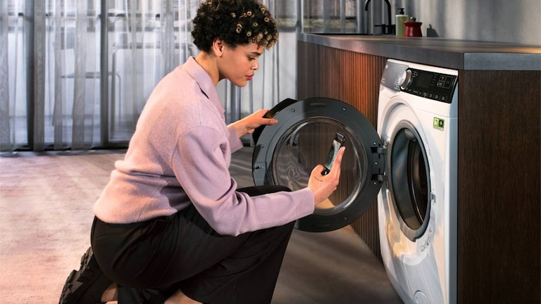 Vrouw kijkt naar telefoon terwijl ze wasmachine opent