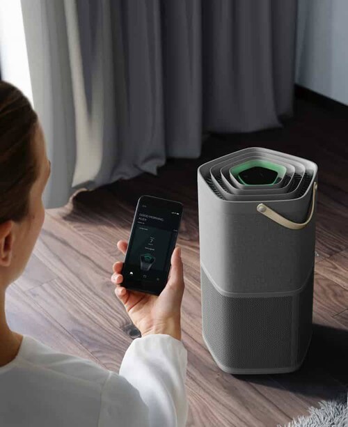 Een vrouw met haar smartphone voor een luchtzuiveraar