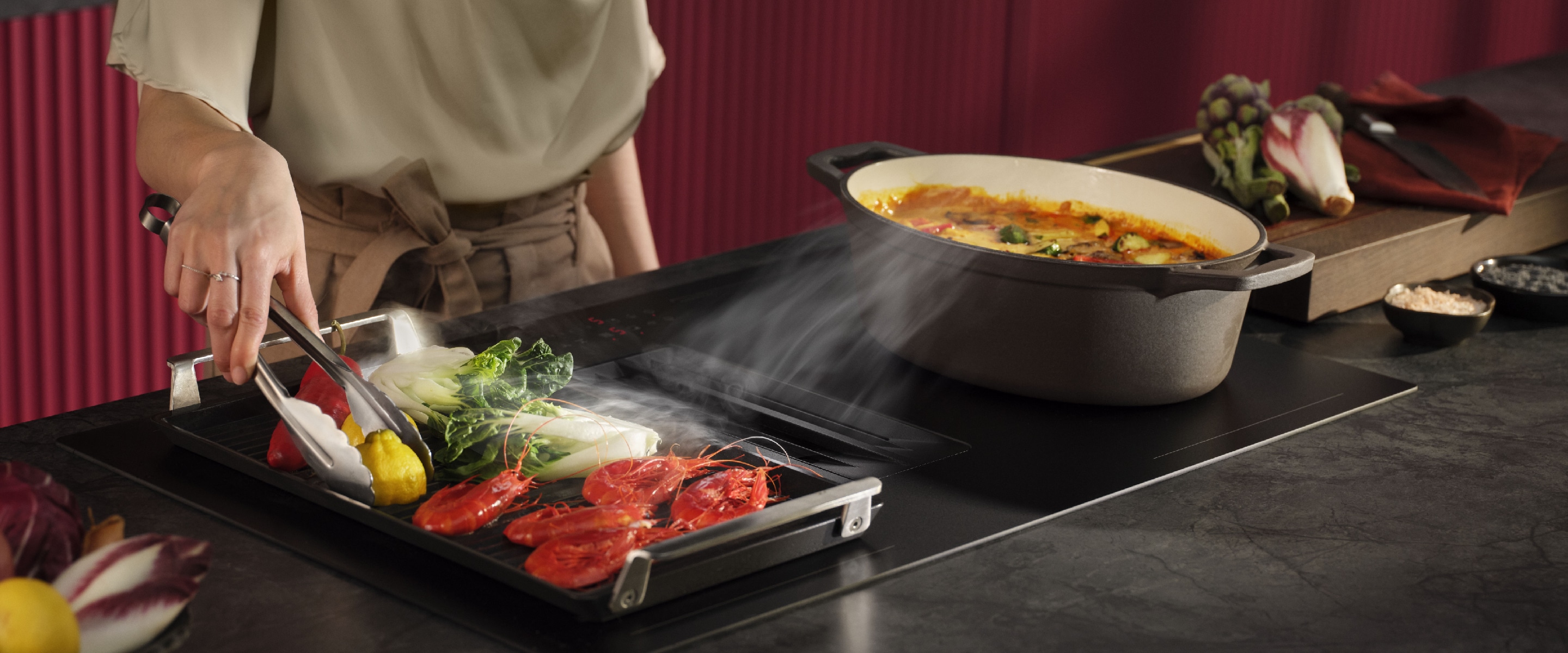 Vrouw die in de keuken staat bij een AEG SaphirMatt® kookplaat met afzuiging