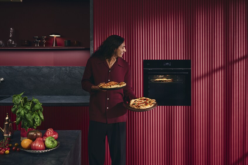 Vrouw die een pizza vasthoudt bij de oven