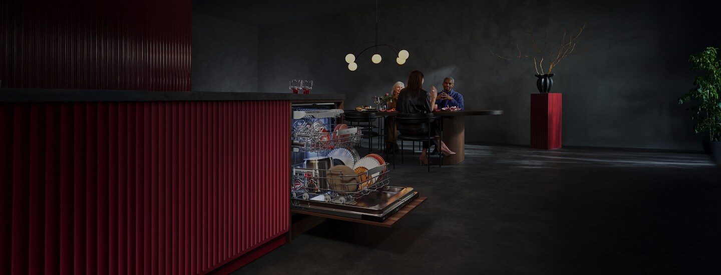 Im Vordergrund steht ein FAVORIT Geschirrspüler mit geöffneter Türe, im Hintergrund sitzen Personen an einem Tisch und unterhalten sich