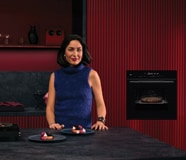 Vrouw in een keuken voor een bordeauxrode wand waar een ingebouwde zwart AEG 8000 serie heteluchtoven met magnetron