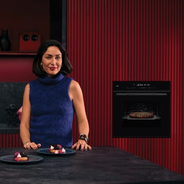 Vrouw in een keuken voor een bordeauxrode wand waar een ingebouwde zwart AEG 8000 serie heteluchtoven met magnetron